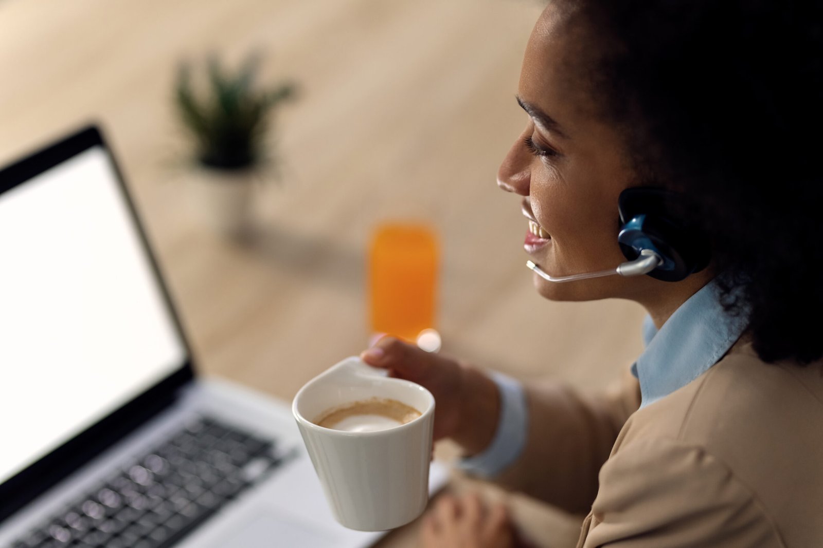 Happy black businesswoman using laptop and having conference call while enjoying in cup of coffee in the office.